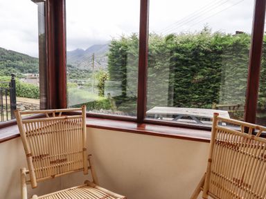 Two wooden chairs inside a room with large windows showing a green hedge and mountain view at Haulfryn in Bethesda