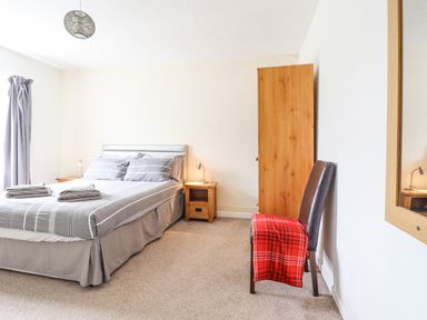 A bedroom with a double bed gray bedding two bedside tables lamps wooden wardrobe chair with red blanket and wall mirror at Haulfryn Bethesda