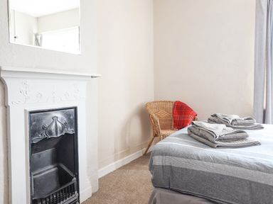 A bedroom with a bed with folded towels a wicker chair with a red blanket and a small fireplace at Haulfryn in Bethesda