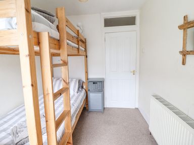 A bedroom with a wooden bunk bed a small cabinet a white door and a radiator at Haulfryn in Bethesda