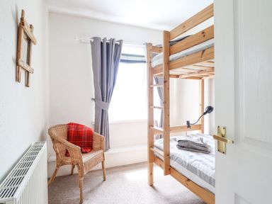 A bedroom with a wooden bunk bed a wicker chair with a red blanket a window with gray curtains and a wall mirror at Haulfryn in Bethesda