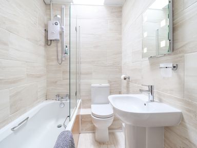A bathroom with a bathtub shower unit toilet sink and mirror at Haulfryn in Bethesda