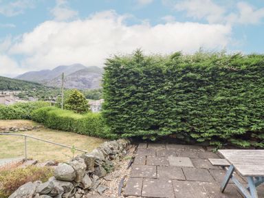 A garden area with a stone wall hedge and a wooden table with benches outside at Haulfryn in Bethesda