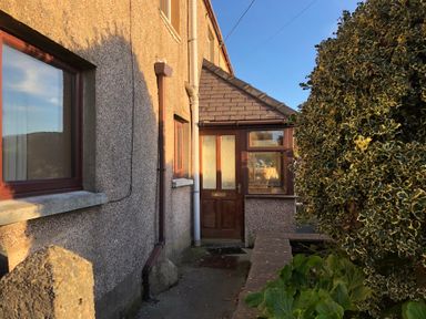 A pathway leading to a wooden door with glass panels on a house with pebble dash walls and a bush nearby at Haulfryn in Bethesda