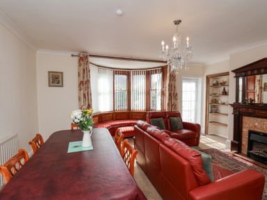 A room with a dining table and chairs a red leather sofa a bay window and a fireplace at Mayfield Manor in Whitby