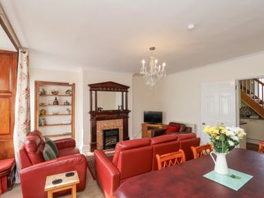 A living room with red sofas a wooden fireplace a chandelier and a dining table with flowers at Mayfield Manor in Whitby