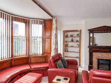 A living room with red leather sofas a wooden built in bookshelf a fireplace and a curved window seating area at Mayfield Manor in Whitby