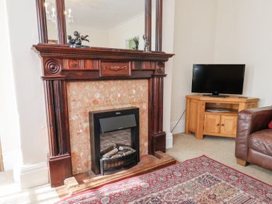A room with a wooden fireplace and a television on a wooden stand at Mayfield Manor in Whitby