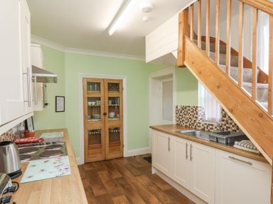 A kitchen with a wooden floor white cabinets green walls a staircase and a wooden door at Mayfield Manor in Whitby