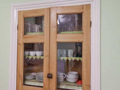 A wooden kitchen cabinet with glass doors containing white cups bowls and plates at Mayfield Manor in Whitby