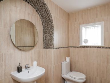 A bathroom with a white sink and a round mirror above it a toilet with a roll of toilet paper and a window with a small circular mirror on the sill at Mayfield Manor in Whitby