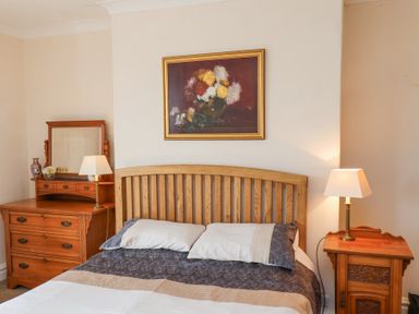 A bedroom with a wooden bed headboard two bedside tables with lamps a dresser with a mirror and a painting above the bed at Mayfield Manor in Whitby