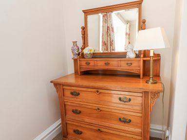 A wooden dresser with a mirror a lamp a vase with flowers and a small sculpture at Mayfield Manor in Whitby
