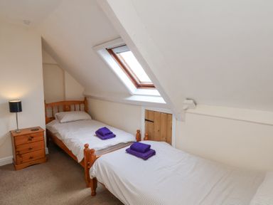 A bedroom with two single wooden beds each with folded purple towels on top and a wooden nightstand with a lamp under a skylight window at Mayfield Manor in Whitby