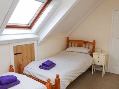A bedroom with two single wooden beds with striped bedding and purple towels under a skylight window at Mayfield Manor in Whitby
