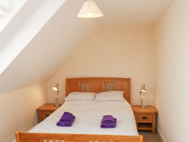 A bedroom with a wooden double bed with white bedding and two purple towels on the bed at Mayfield Manor in Whitby