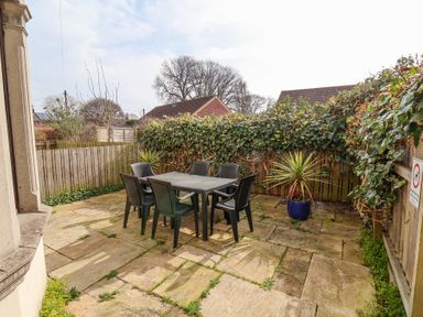 An outdoor patio area with a table and six chairs surrounded by a wooden fence and plants at Mayfield Manor in Whitby