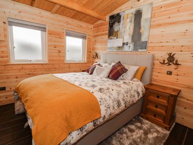 A bedroom with a bed pillows bedside table and two windows at The Cabin in Pontardawe