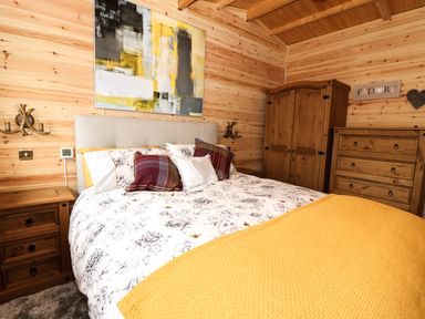 A bedroom with a bed with floral bedding and yellow blanket wooden furniture and abstract painting at The Cabin in Pontardawe