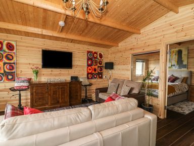 A living room with wooden walls and ceiling a TV above a wooden cabinet a beige sofa a brown sofa and colorful wall art at The Cabin in Pontardawe
