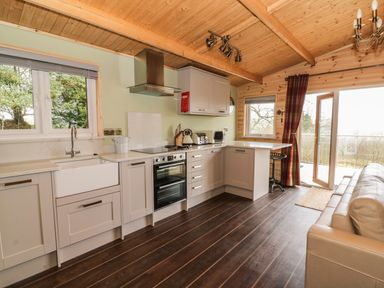 A kitchen with cabinets a sink an oven and stove a bar stool and an open door leading outside at The Cabin in Pontardawe