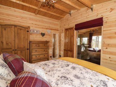 A bedroom with wooden walls and ceiling a bed with patterned bedding wooden furniture and a window with a maroon blind at The Cabin in Pontardawe