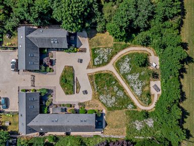 An aerial view of a property with two buildings three parked cars a gravel courtyard garden beds walking paths and green trees at Budmouth Upwey near Weymouth
