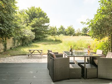 An outdoor seating area with a table and chairs on a deck overlooking a grassy garden with a picnic bench at Shepherd Oak in Upwey near Weymouth