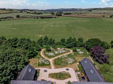 An aerial view of a garden with pathways forming a heart shape between two buildings with fields and hills in the background at Shepherd Oak in Upwey near Weymouth