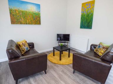 A living room with two brown leather sofas a small black table on a yellow rug a television and colorful paintings at Bramshurst in Upwey near Weymouth