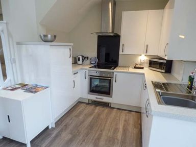 A kitchen with white cabinets an oven a kettle a microwave and a sink at Bramshurst Upwey near Weymouth