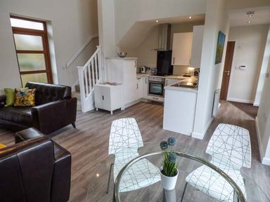 A living room with leather sofas a glass dining table and a kitchen at Bramshurst in Upwey near Weymouth