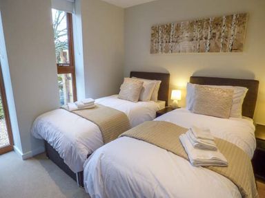 A bedroom with two single beds with beige runners and towels by a window at Bramshurst in Upwey near Weymouth