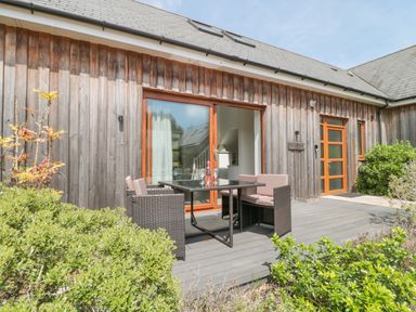 An outdoor patio with a wicker table and chairs in front of a wooden house at Bramshurst Upwey near Weymouth