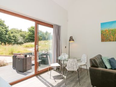 A dining area with a round glass table and four white chairs next to sliding glass doors showing an outdoor patio at Bramshurst in Upwey near Weymouth