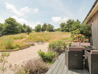 An outdoor patio with a dining table and chairs beside a gravel path and grassy field with trees at Bramshurst in Upwey near Weymouth