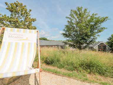 A large chair with text North Manor Meadow in front of grass and trees near a building with multiple windows