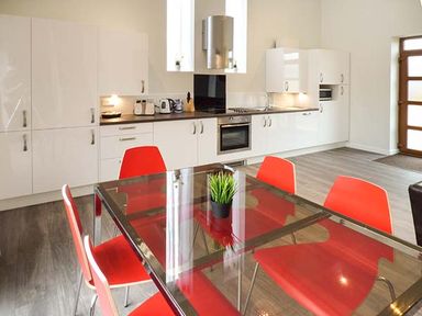 A kitchen with white cabinets and black countertop with a glass dining table and red chairs at Casterbridge in Upwey near Weymouth