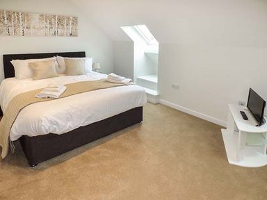A bedroom with a double bed cushions and folded towels a skylight window and a small TV on a white stand at Casterbridge Upwey near Weymouth