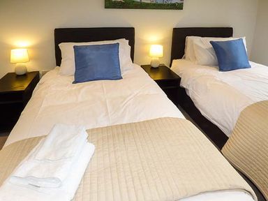 A bedroom with two single beds with blue pillows and beige covers at Casterbridge in Upwey near Weymouth