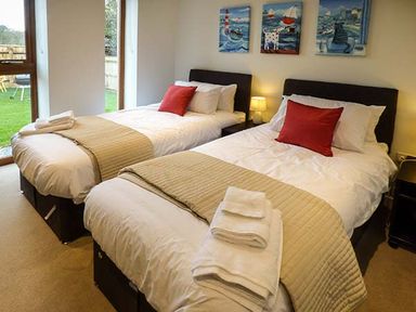 A bedroom with two single beds each with beige bed runners and red pillows at Casterbridge Upwey near Weymouth