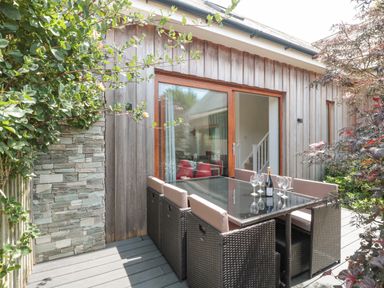 An outdoor patio area with a glass top table surrounded by six wicker chairs and a sliding glass door at Casterbridge in Upwey near Weymouth