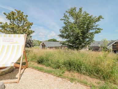 A meadow with tall grass and trees next to modern houses and a chair marked North Manor Meadow at Casterbridge Upwey near Weymouth