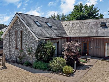 An exterior view of a house with a stone and wooden facade surrounded by plants and trees at Casterbridge Upwey near Weymouth