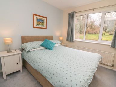 A bedroom with a bed with patterned bedding two bedside tables with lamps a framed picture on the wall and a window with curtains at Trederwen in Rhayader