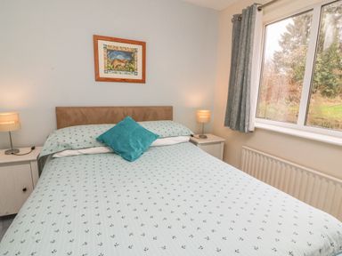 A bedroom with a bed with patterned bedding two bedside tables with lamps a framed picture on the wall and a window with curtains at Trederwen in Rhayader