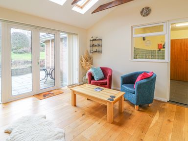 A sitting area with two chairs and a wooden table next to glass doors with a garden view at Trederwen in Rhayader