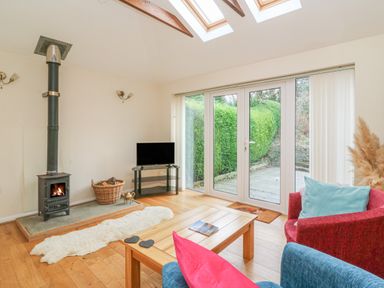 A living room with wood-burning stove a television glass door leading outside and wooden coffee table at Trederwen in Rhayader