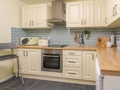 A kitchen with white cabinets wooden countertops a microwave oven stovetop oven utensils and a chair at Trederwen Rhayader