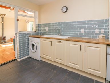 A kitchen with light-colored cabinets a washing machine a sink and blue tiled backsplash at Trederwen in Rhayader